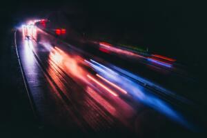 Foto em superexposição, evidenciando luzes de carros em movimento na curva de uma avenida à noite