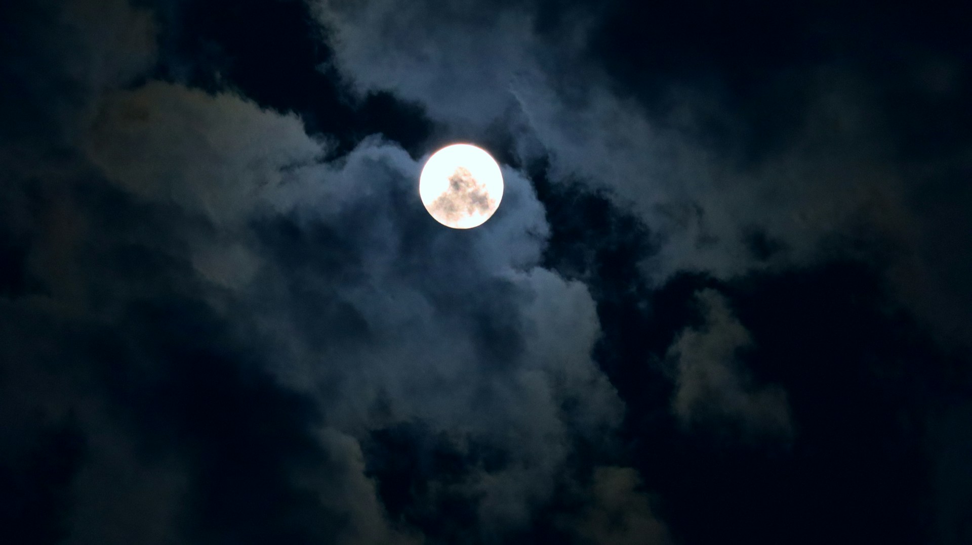 Foto da lua cheia brilhando entre as nuvens