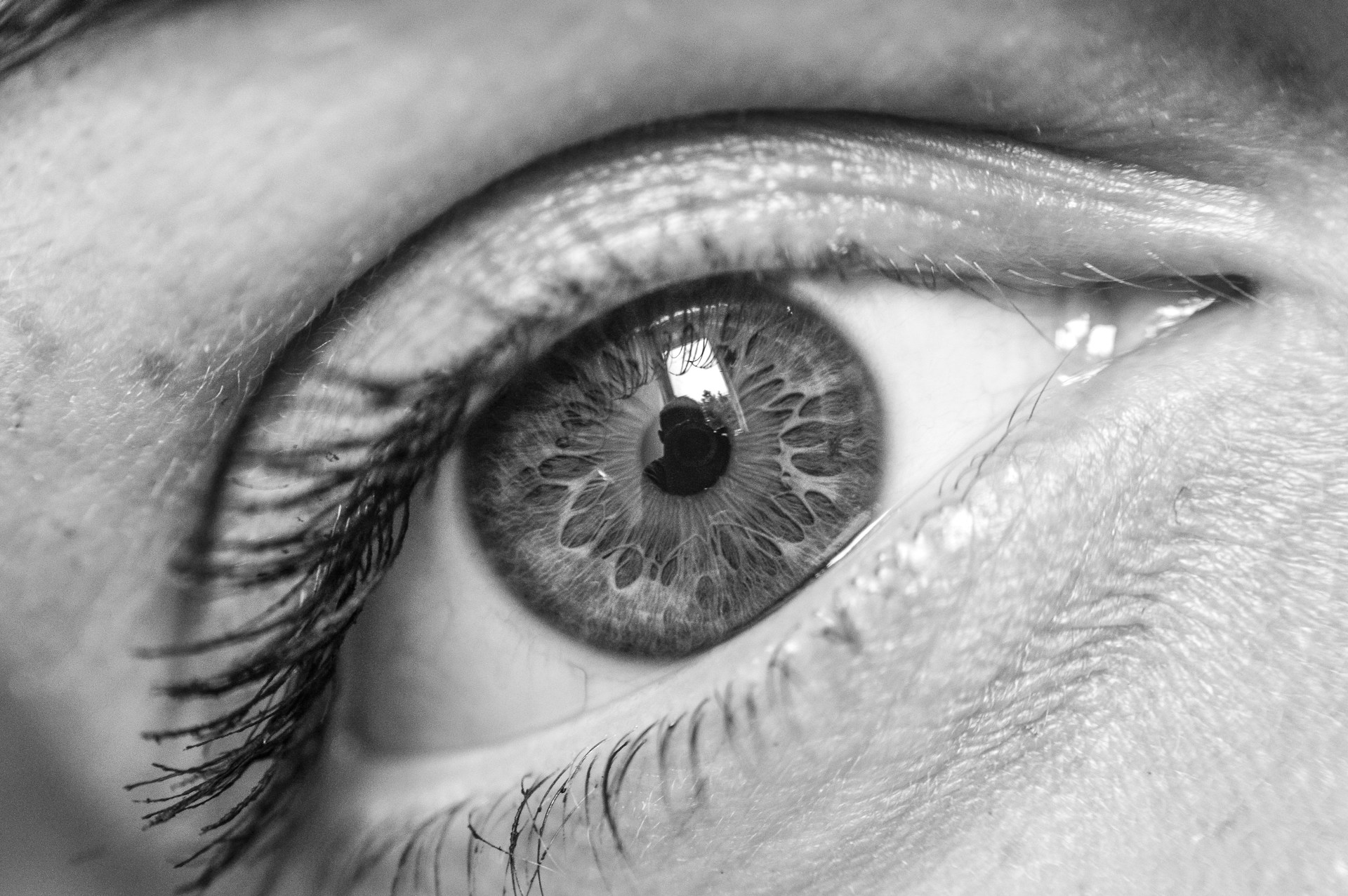 Foto em preto e branco bem aproximada de um olho, realçando detalhes da íris e o reflexo de uma janela e do fotógrafo