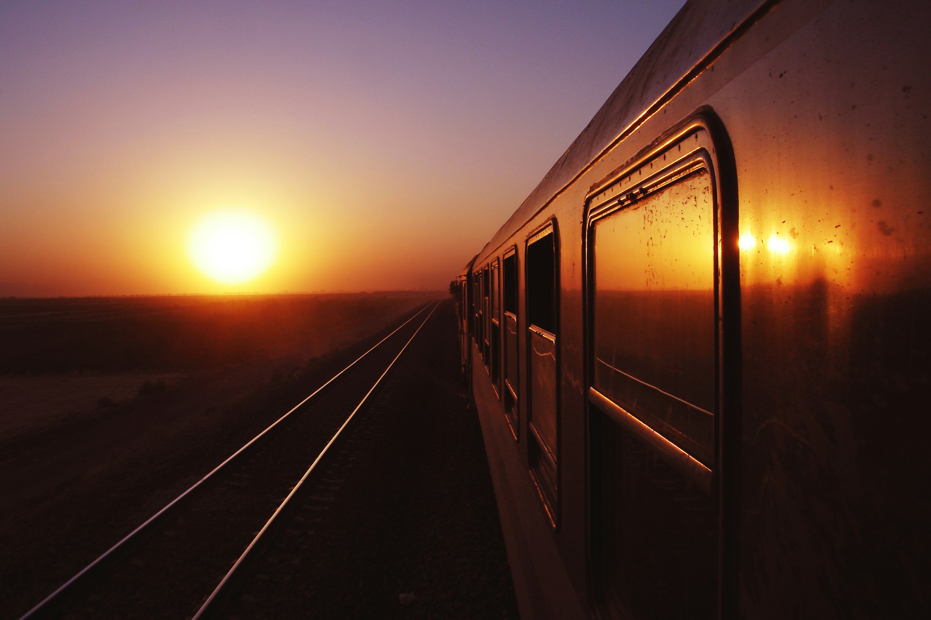 Foto da lateral de um trem em direção ao sol no horizonte